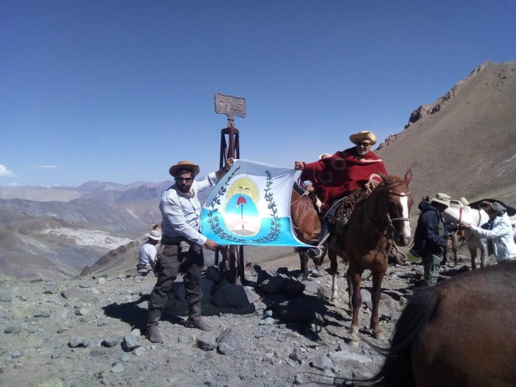 Dos personas muestra bandera del ejercito de San Martín en el límite de Argentina con Chile. Es la finalización de la cabalgata del cruce de los andes.