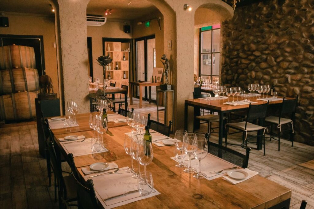 Salón interior de Casa Vigil El Enemigo con arquitectura de piedra, barricas de vino y mesas preparadas para almuerzo gourmet en Maipú
