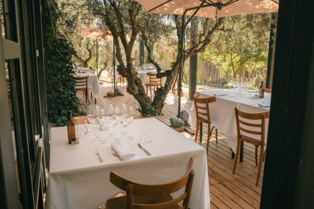 Mesa vestida en la galería exterior y deck con olivos de Casa Vigil El Enemigo para almuerzo maridado en Maipú Mendoza